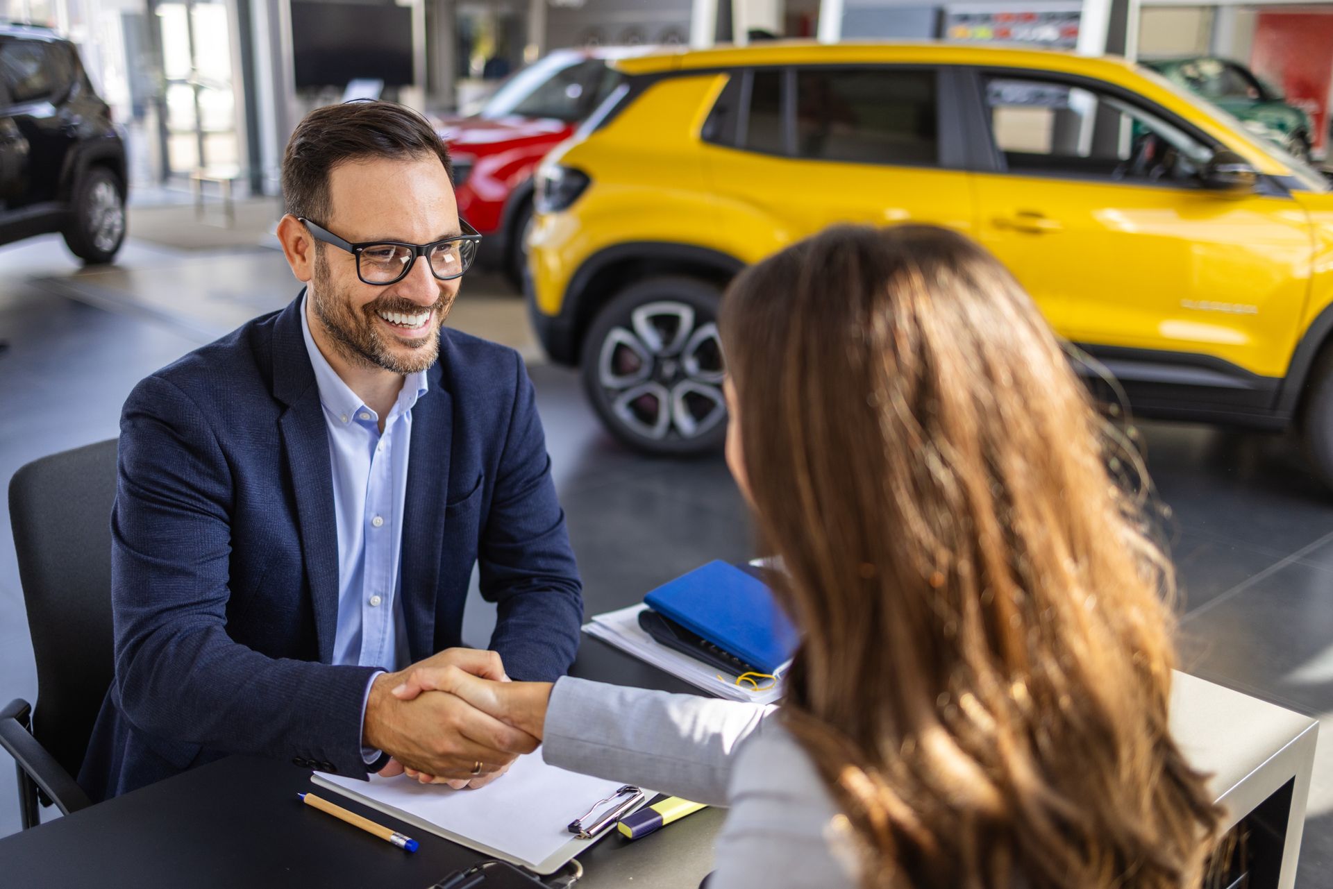 Two people shaking hands at a car dealership, with a yellow car in the background. Two people shaking hands at a car dealership, with a yellow car in the background.