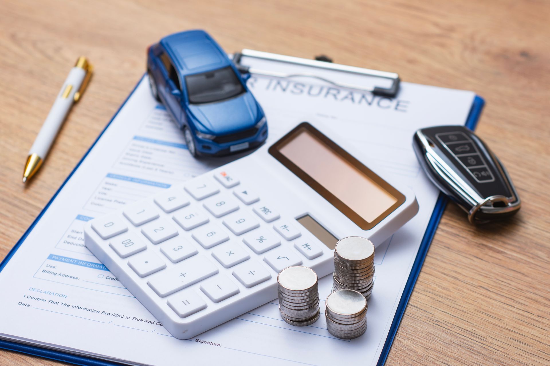 Blue toy car, calculator, coins, and car insurance paperwork, representing vehicle coverage costs.