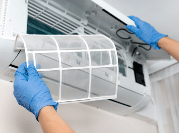 Hands in blue gloves removing an air conditioner filter.