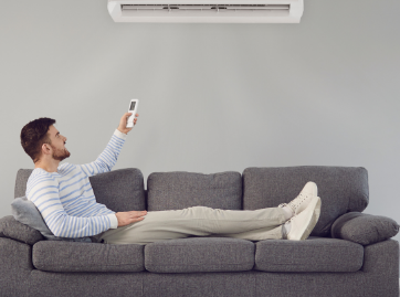 Man on couch using AC remote in a gray room.