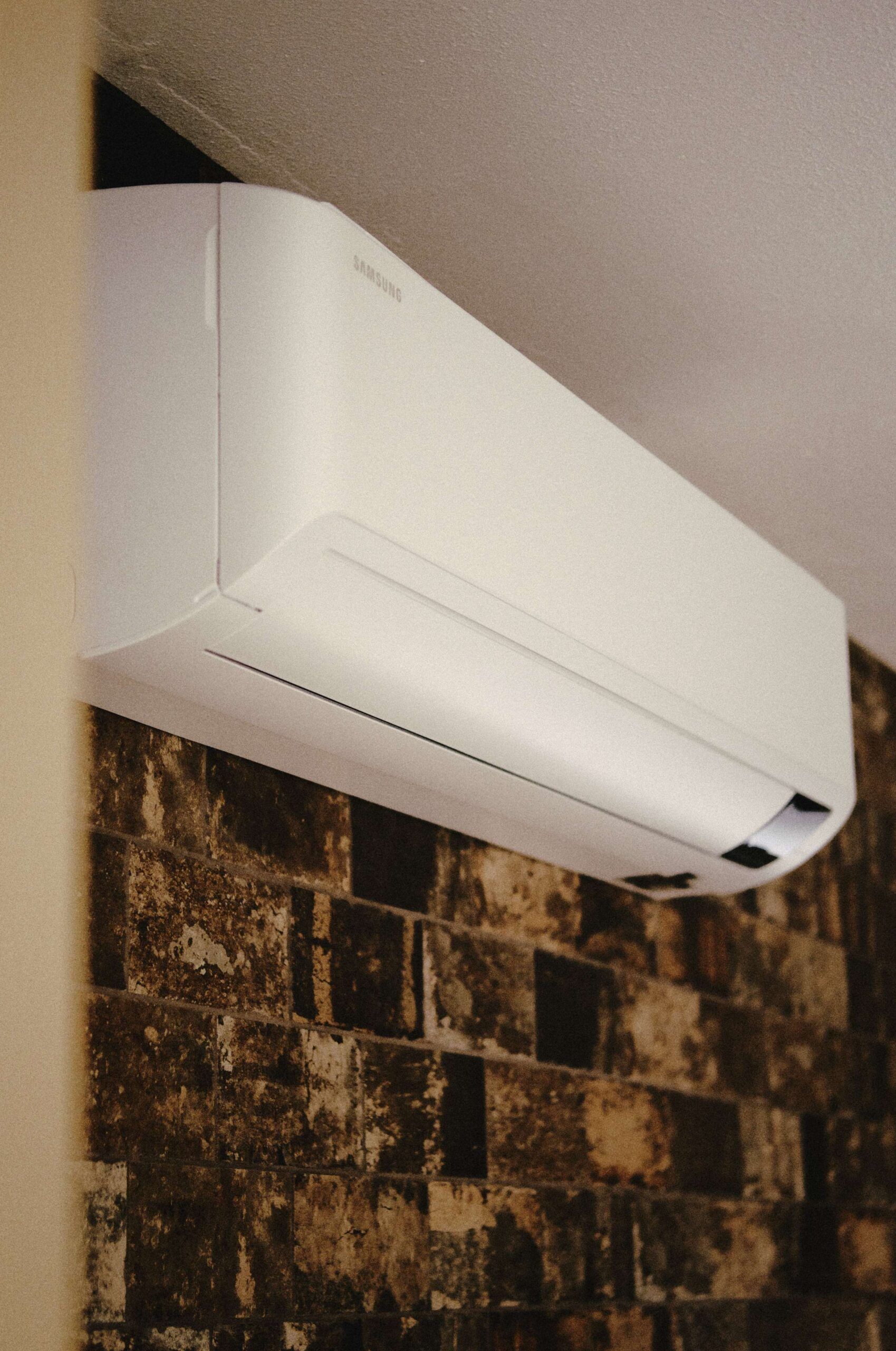 White wall-mounted air conditioning unit on a patterned brick wall.