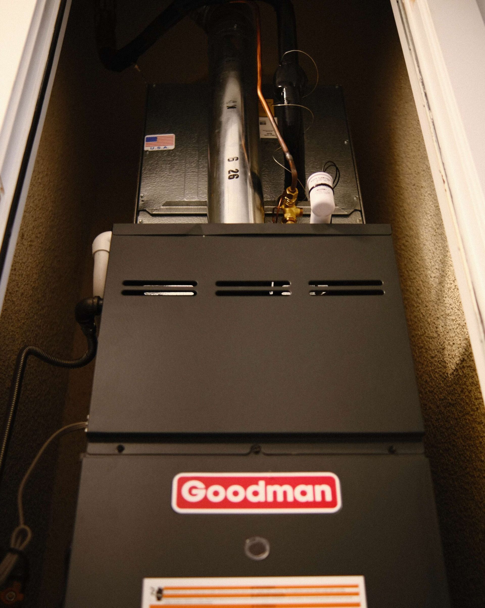 Goodman furnace in a recessed closet; black and gray with red logo.