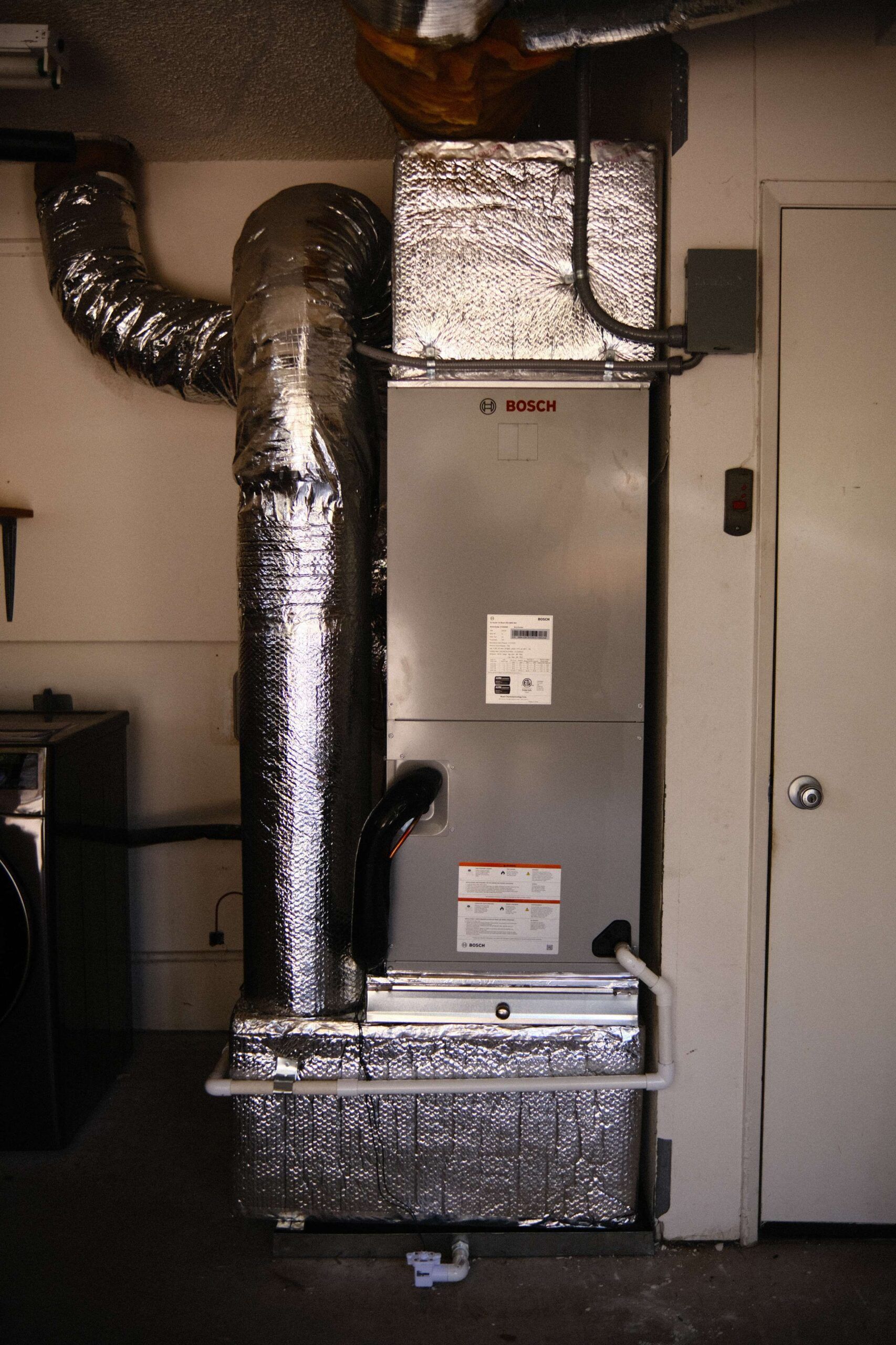 Furnace unit with silver ductwork in a utility room.