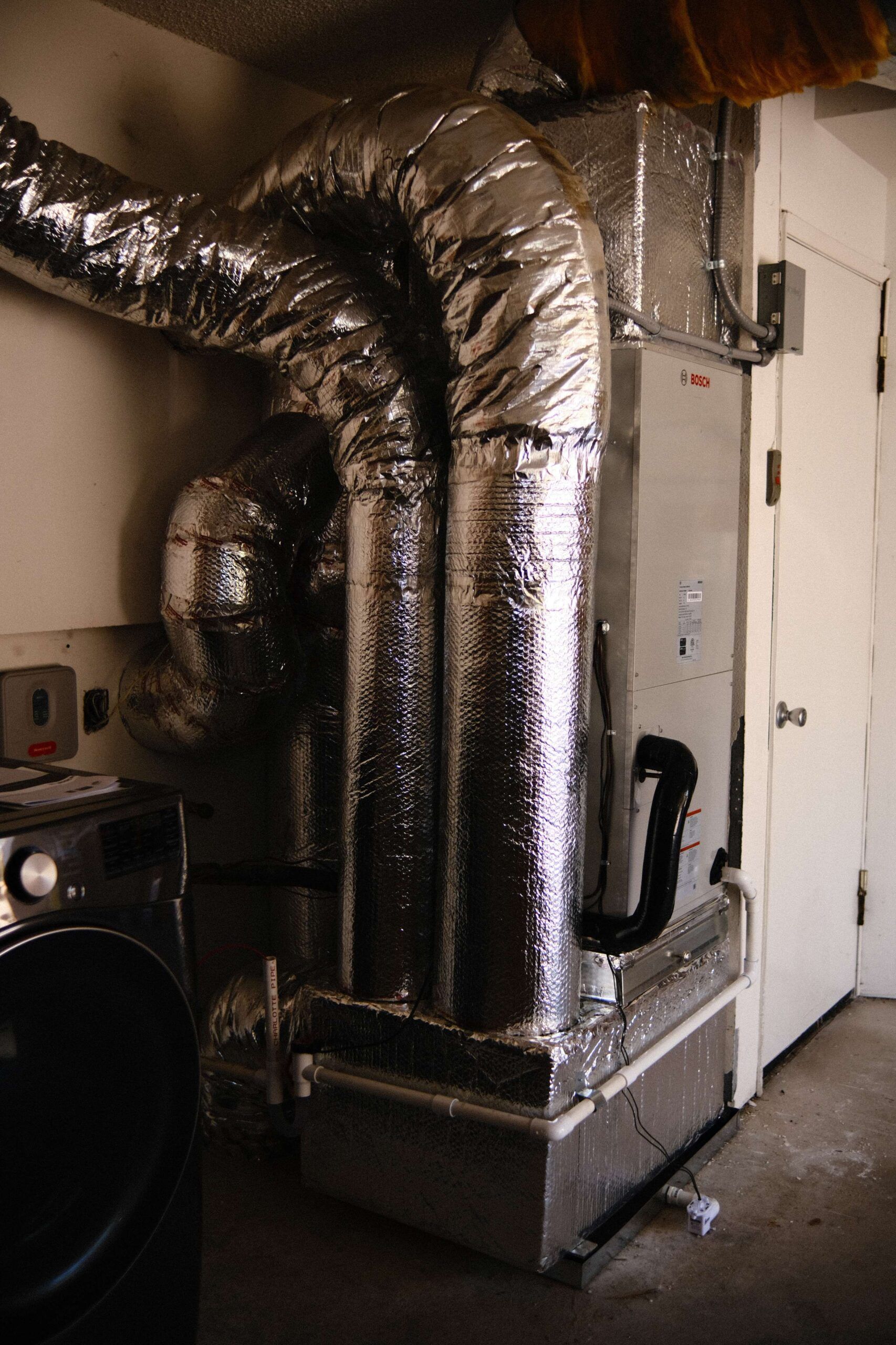 HVAC unit with insulated ductwork, installed near a laundry area with a washing machine and door.