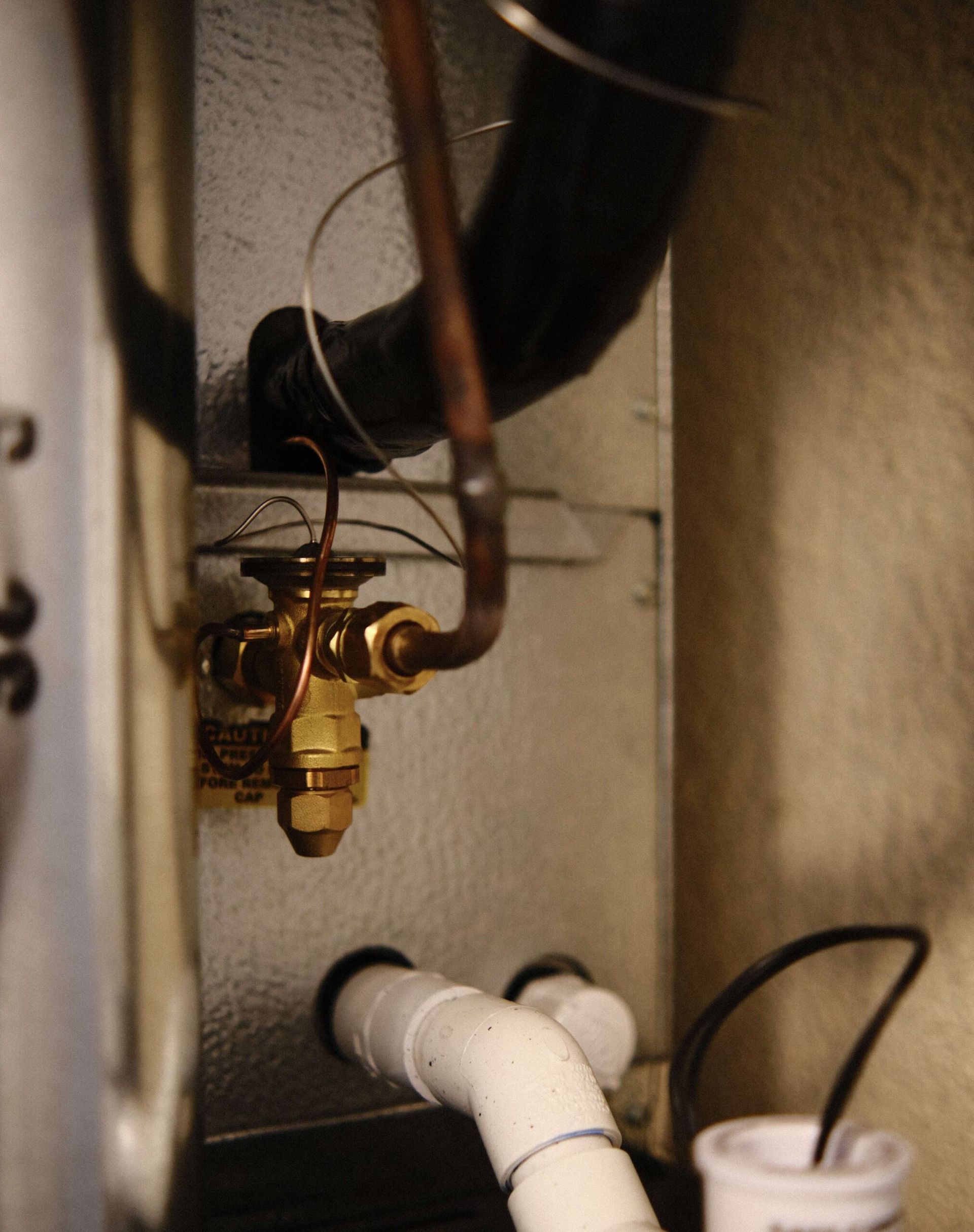 Close-up of HVAC system components: copper pipes, valve, insulation, and condensation drain tubes.