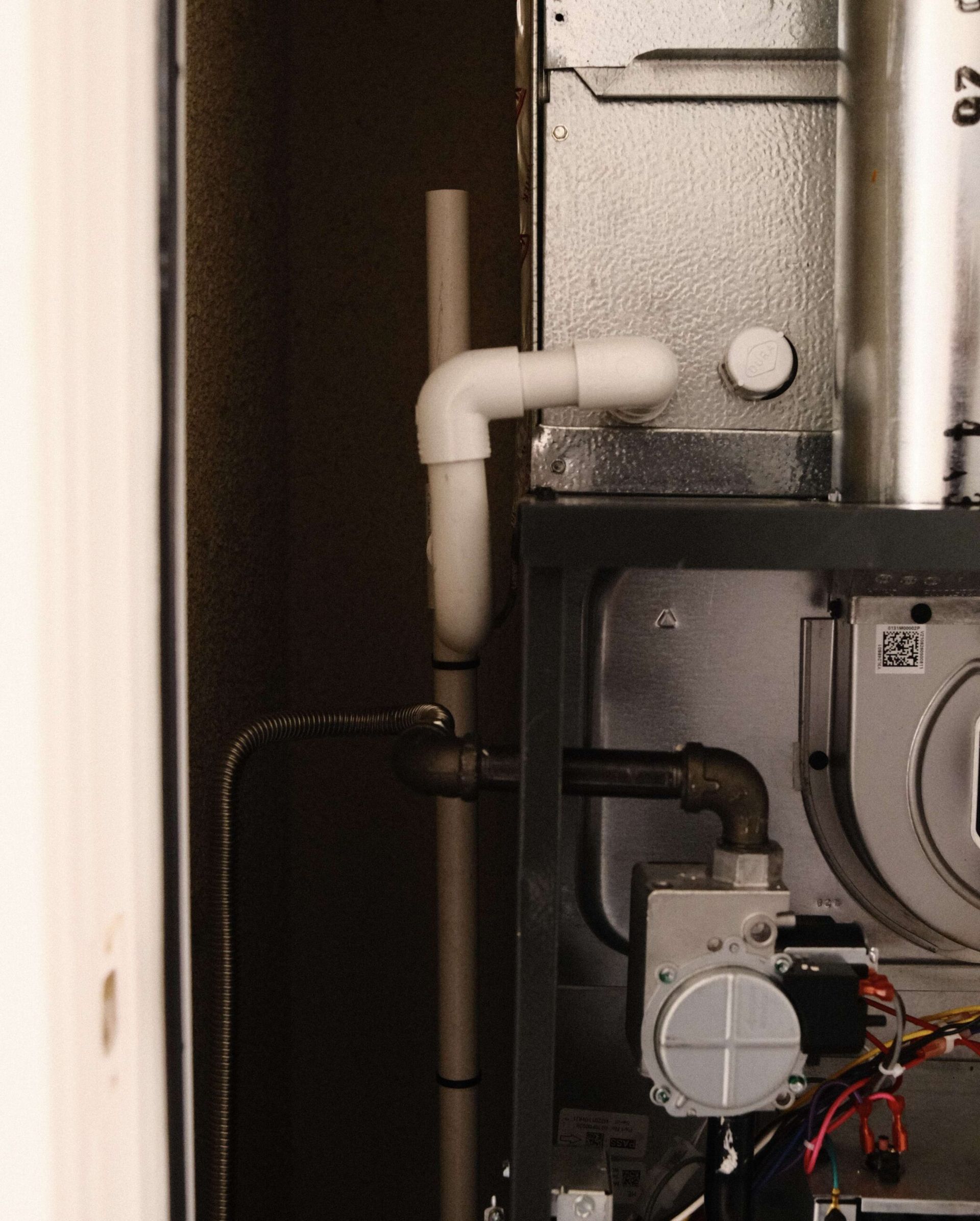 Furnace with white PVC pipe, elbows, and metal components in a wooden enclosure.