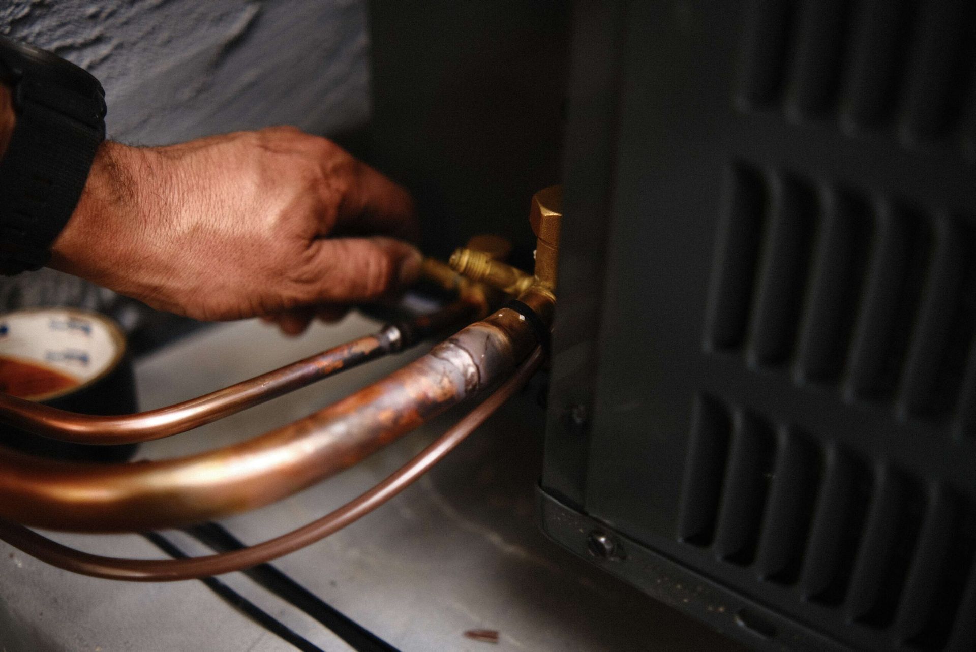 Person using a wrench to adjust copper pipes connected to an air conditioning unit.