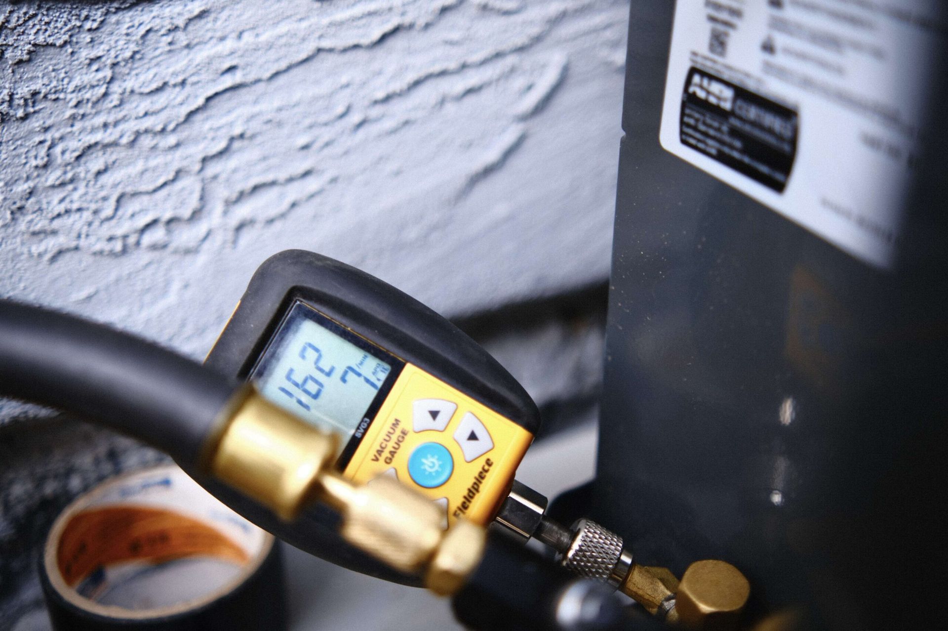 Digital gauge connected to an air conditioning unit; screen displays pressure reading.