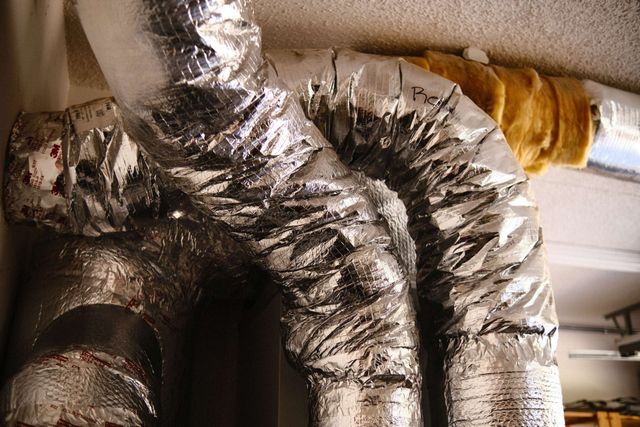 Silver insulated air ducts curving across a ceiling. One section is wrapped in yellow insulation.