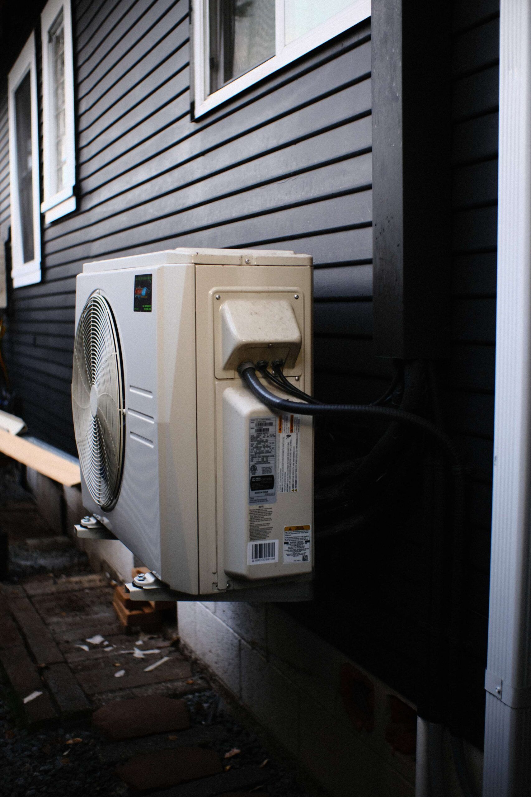 White air conditioning unit mounted on a black building exterior, with electrical cables.