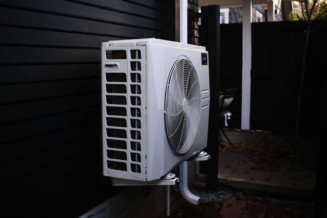 White HVAC unit mounted on a dark exterior wall, with an adjacent black support post.