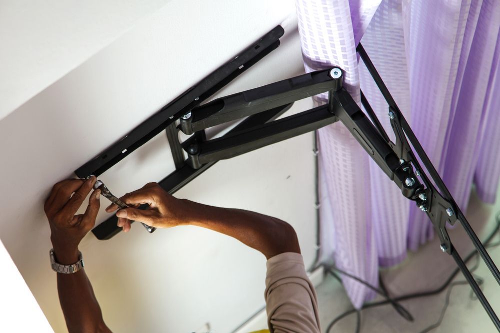 Person Using a Wrench to Mount a Black Tv Bracket to a White wall — Audiomation in Nabiac, NSW