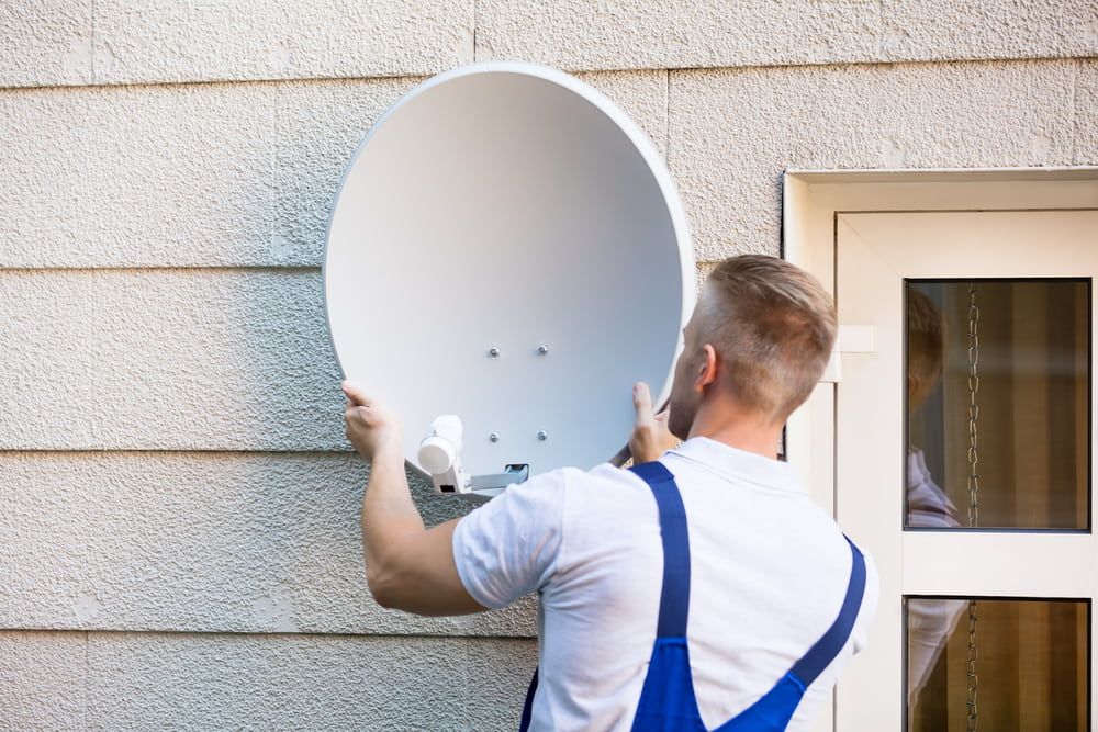 A Man is Installing a Satellite Dish on the Side of a Building — Audiomation in Old Bar, NSW