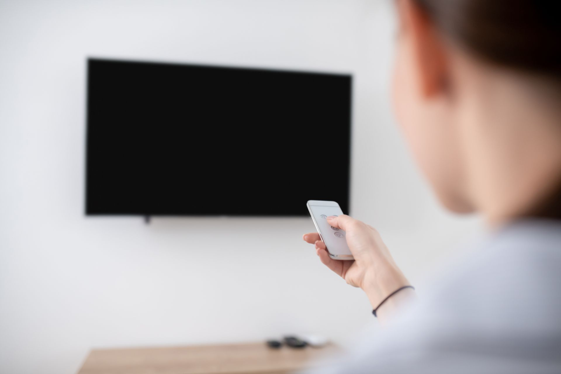 A person pointing a remore to a tv on the wall — Audiomation in Nabiac, NSW