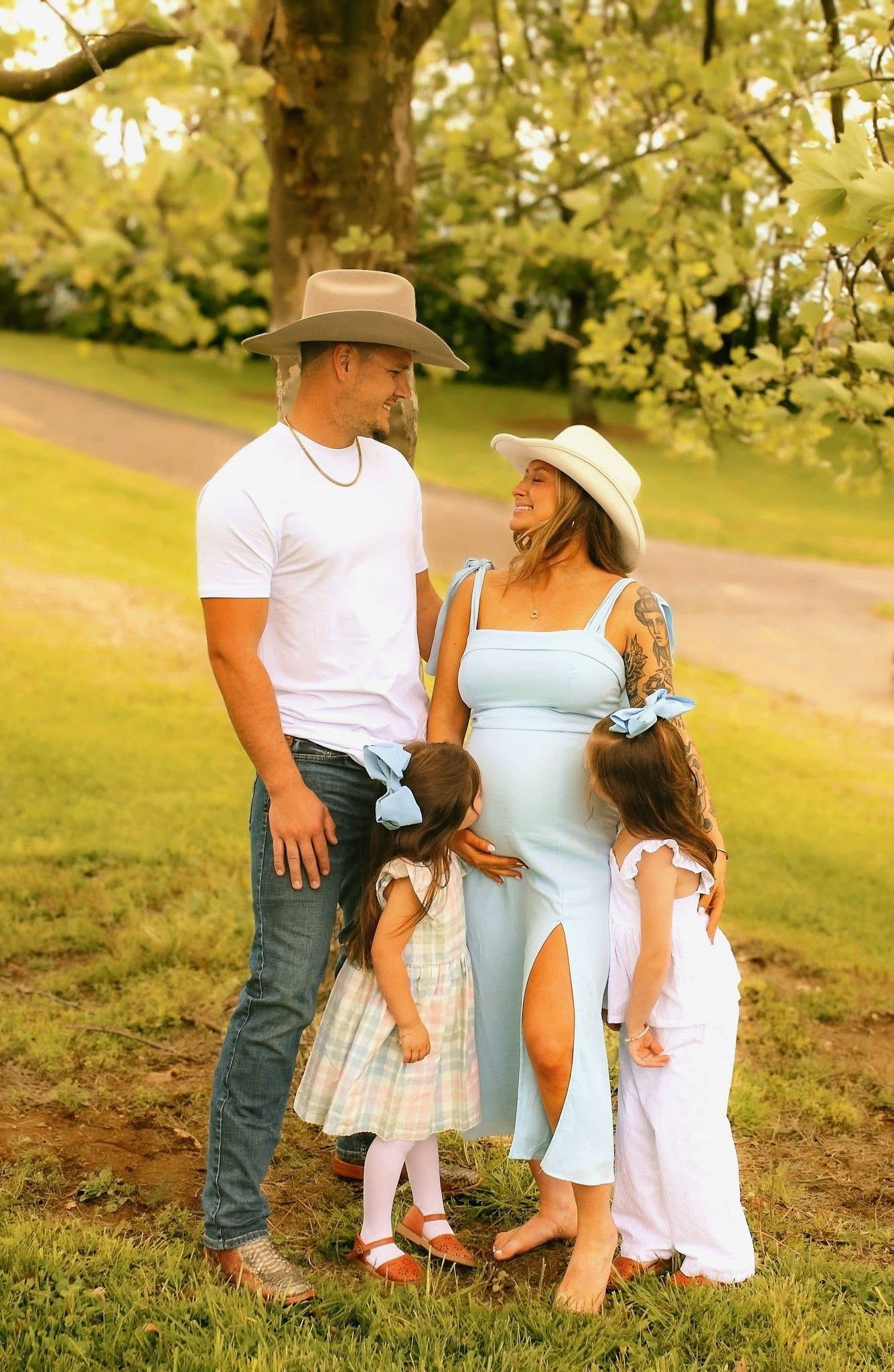 Family standing together outdoors in a grassy park, dressed in light summer clothes and hats.