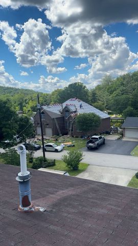 Neighborhood street and house under a bright blue sky with large clouds, viewed from a rooftop.