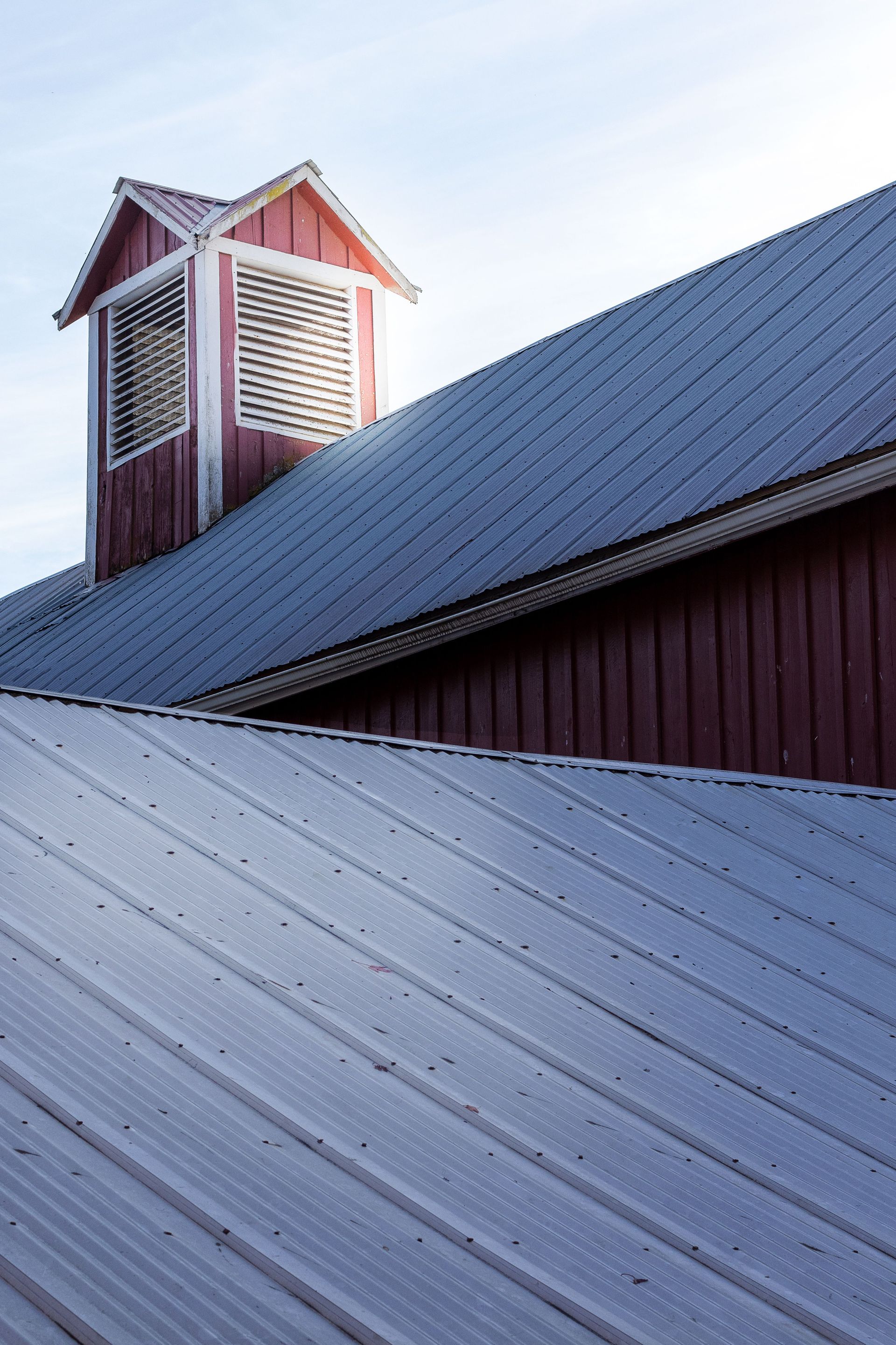 Red barn roof with white cupola and metal siding against a bright sky