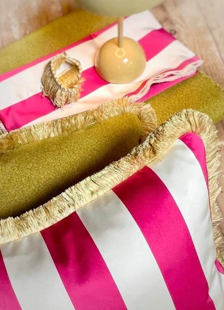 Un cuscino a righe rosa e bianche con frange dorate