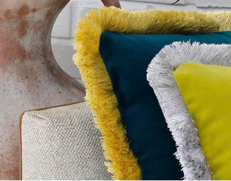 Un cuscino giallo con frange bianche è appoggiato accanto a un cuscino blu