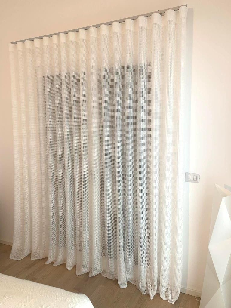 Una tenda bianca è appesa alla finestra di una camera da letto.