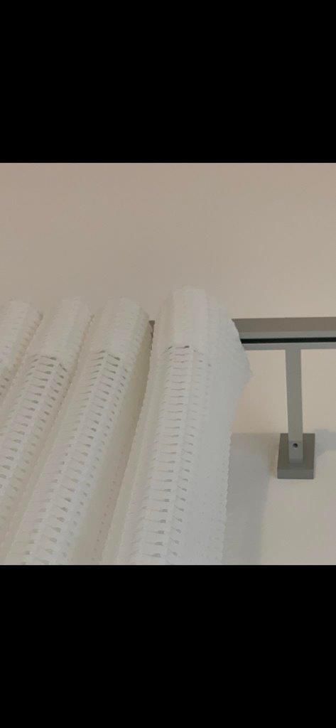 Una tenda bianca è appesa su una parete bianca accanto a una ringhiera di metallo.