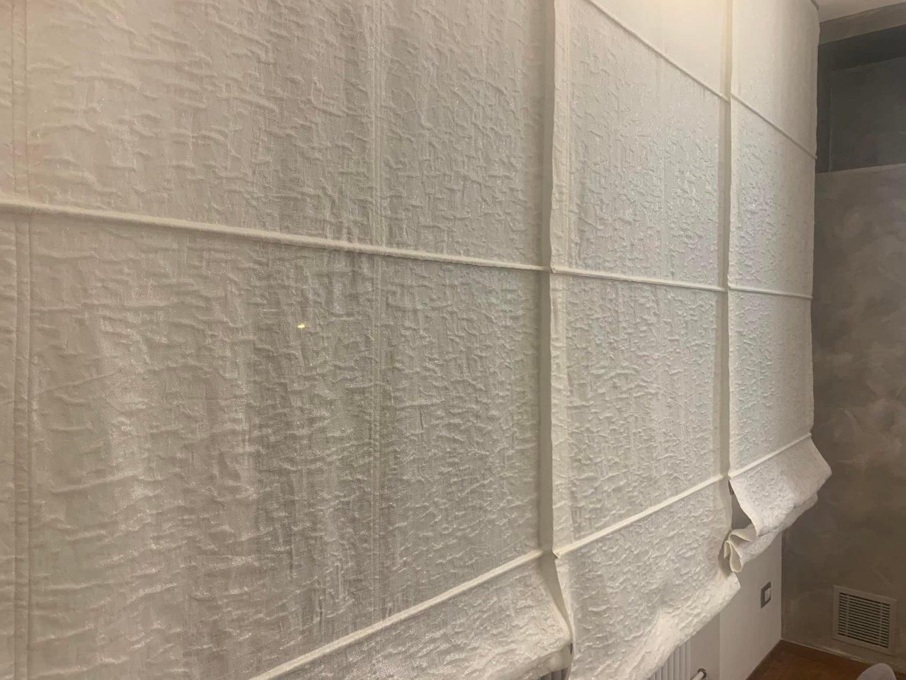 Una tenda romana bianca è appesa alla parete di un bagno.