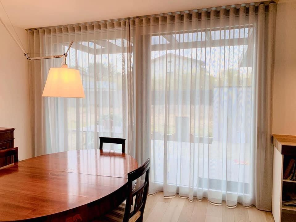 Una sala da pranzo con tavolo, sedie e tende trasparenti.