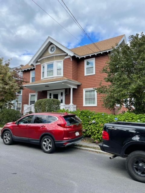 A red car is parked in front of a large red house