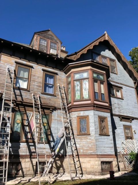 A large house is being painted with ladders in front of it
