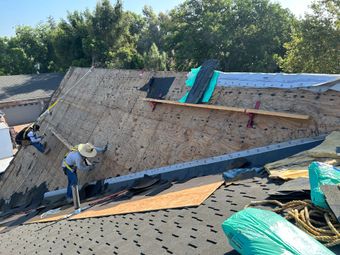 Roofers working on a steep house roof with underlayment exposed and materials stacked nearby