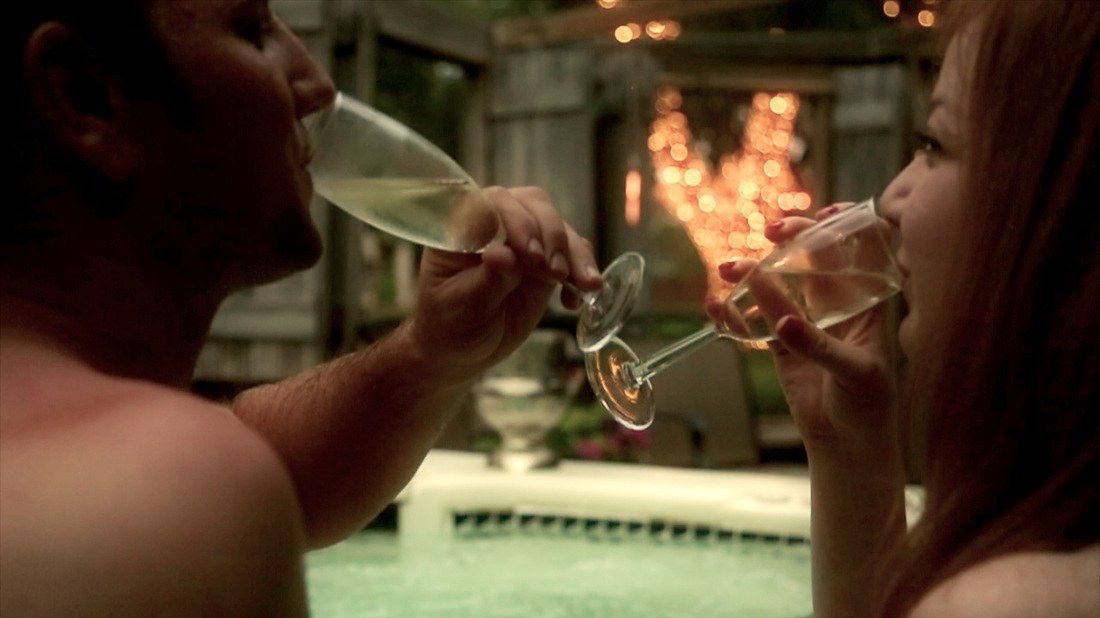 A man and a woman are drinking champagne in a hot tub.