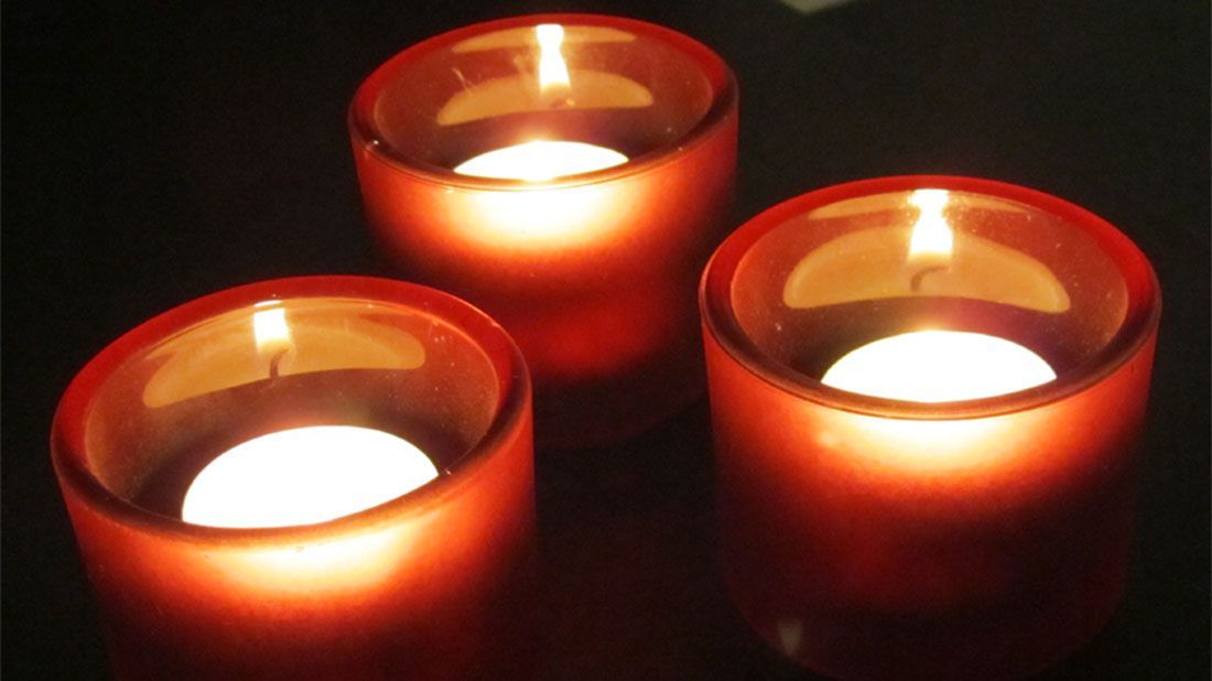 Three red candles are lit up in a dark room