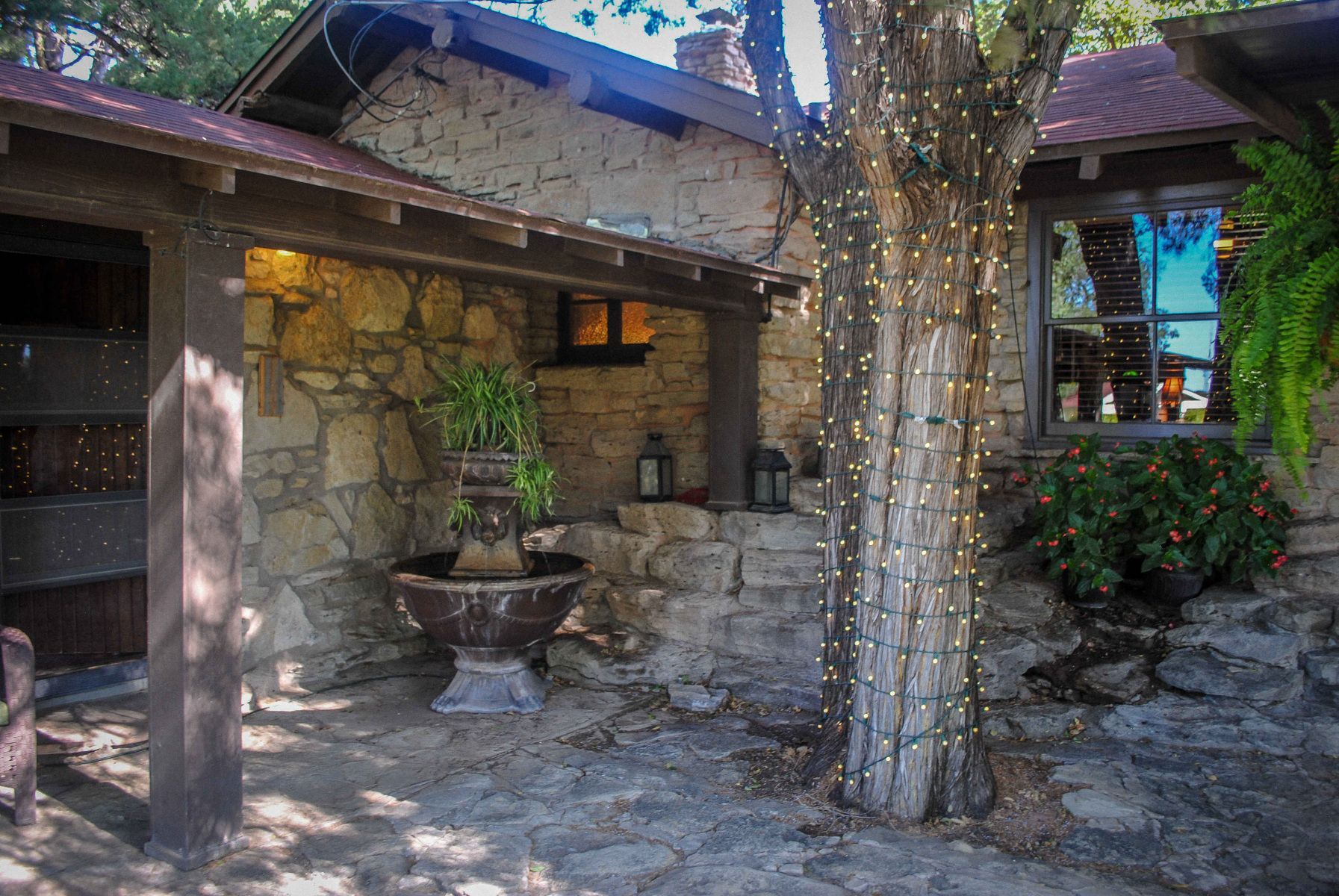 A stone house with a tree and a fountain in front of it.