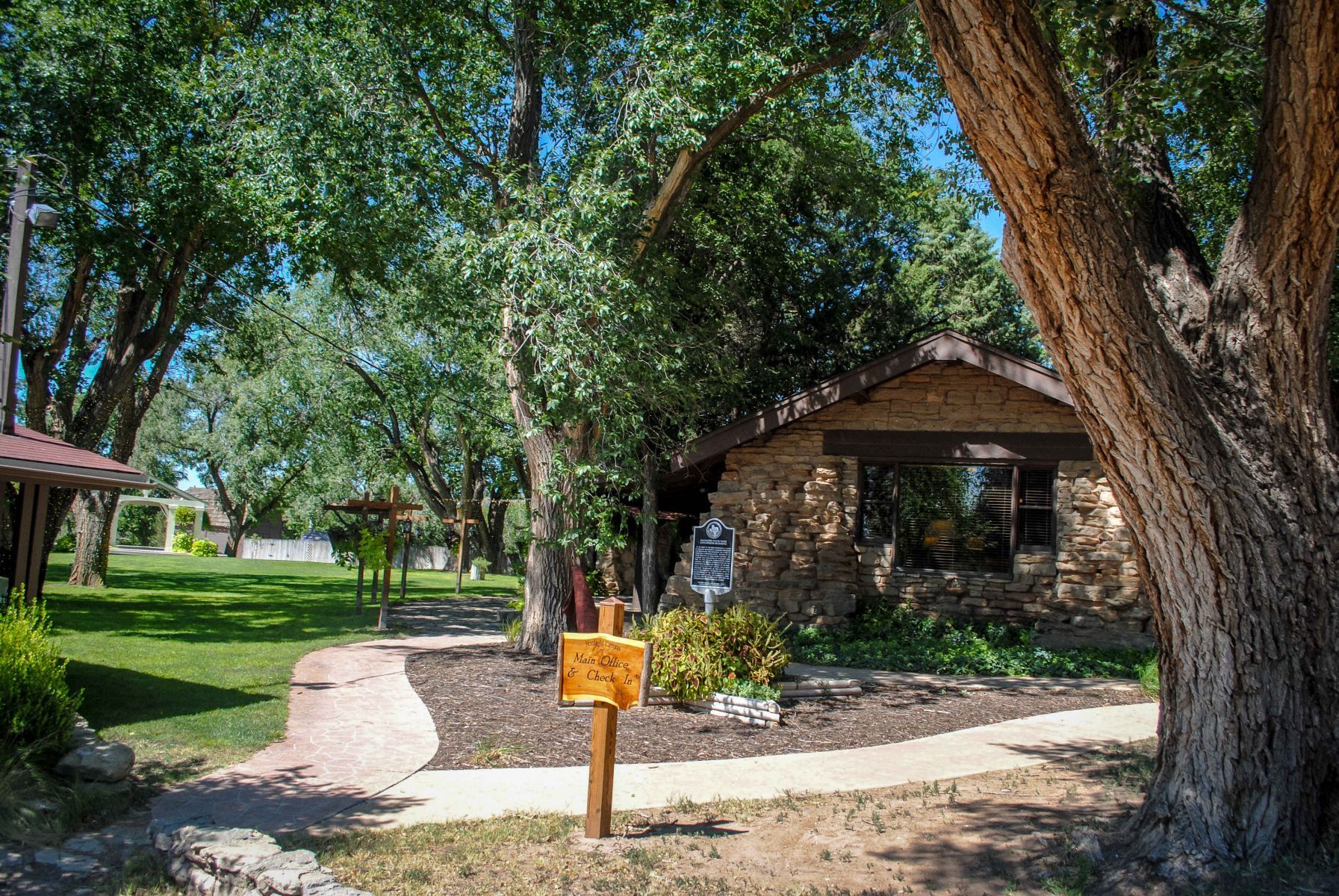 A wooden sign is sitting in front of a house surrounded by trees.