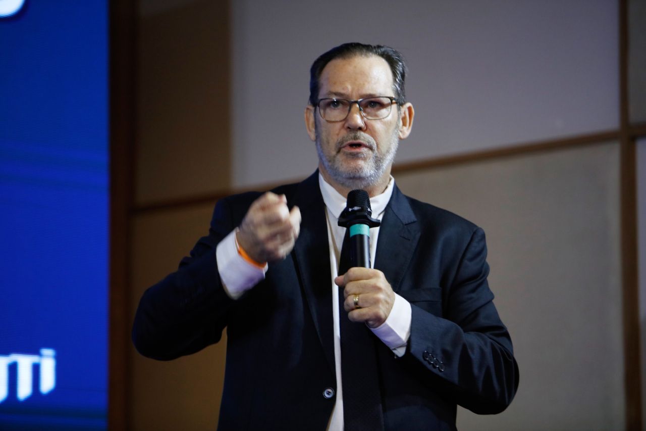 Um homem de terno e gravata está segurando um microfone e apontando.