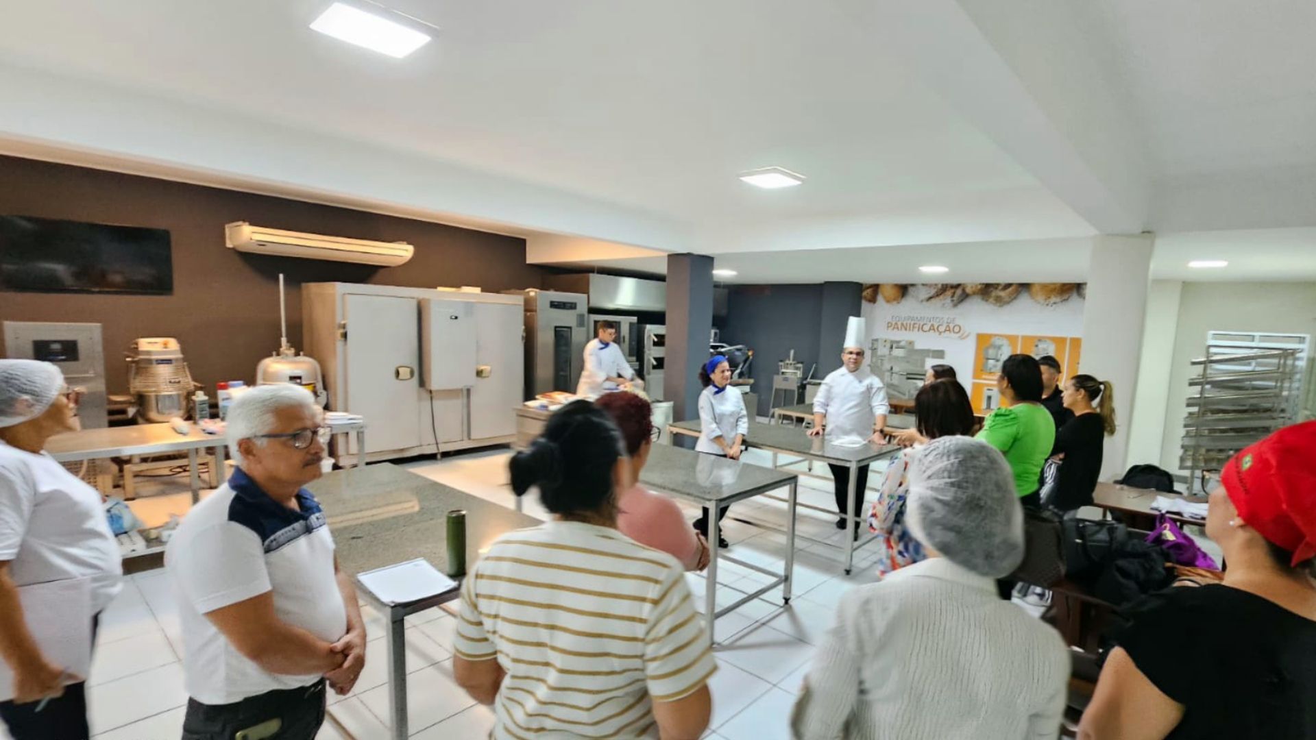 Um grupo de pessoas está em pé ao redor de uma mesa na cozinha.