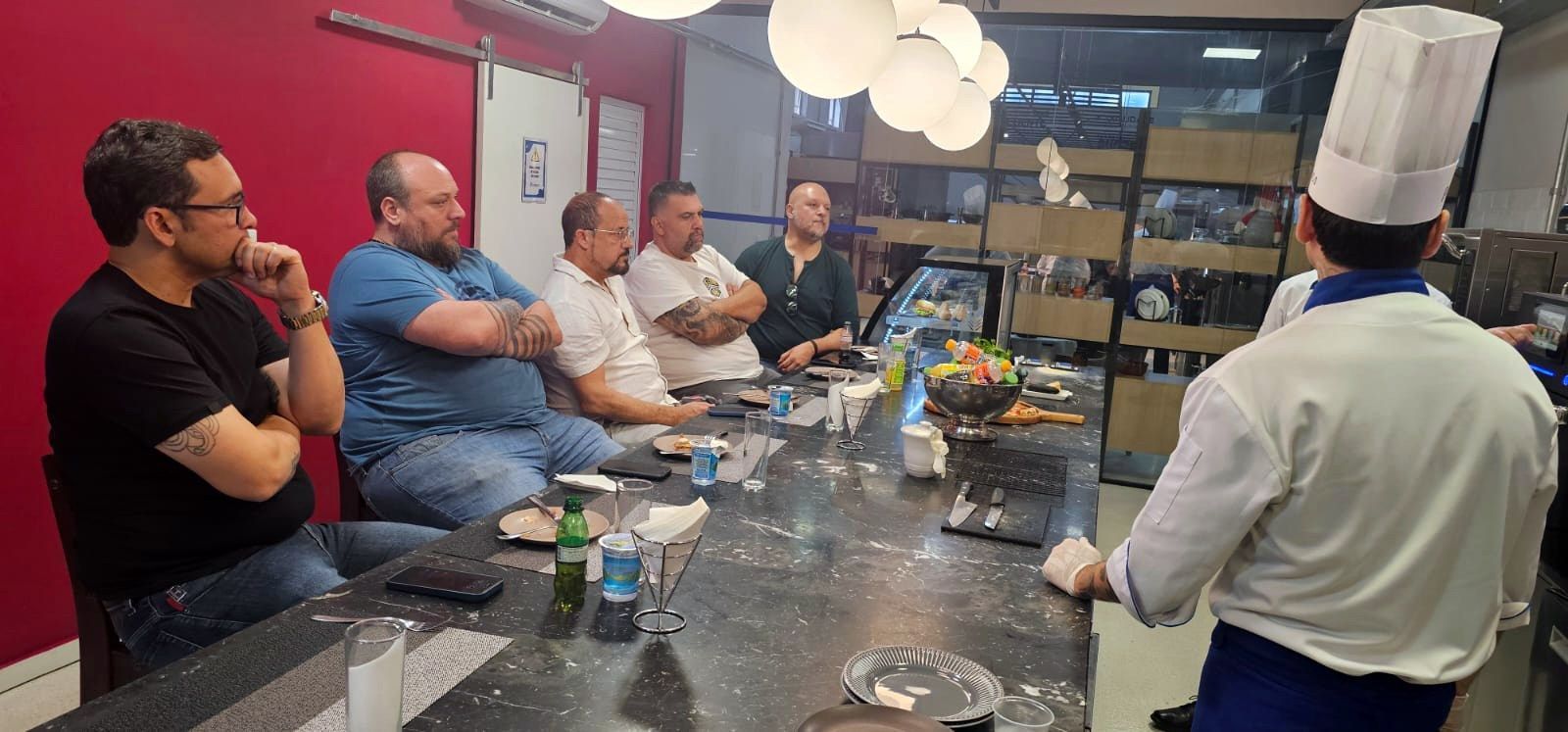 Um grupo de homens está sentado à mesa com um chef em pé na frente deles.