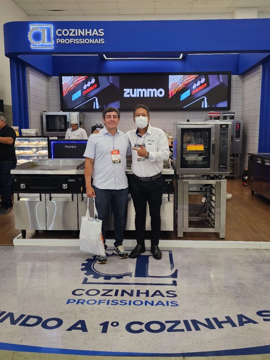 Dois homens parados em frente a uma placa que diz zummo