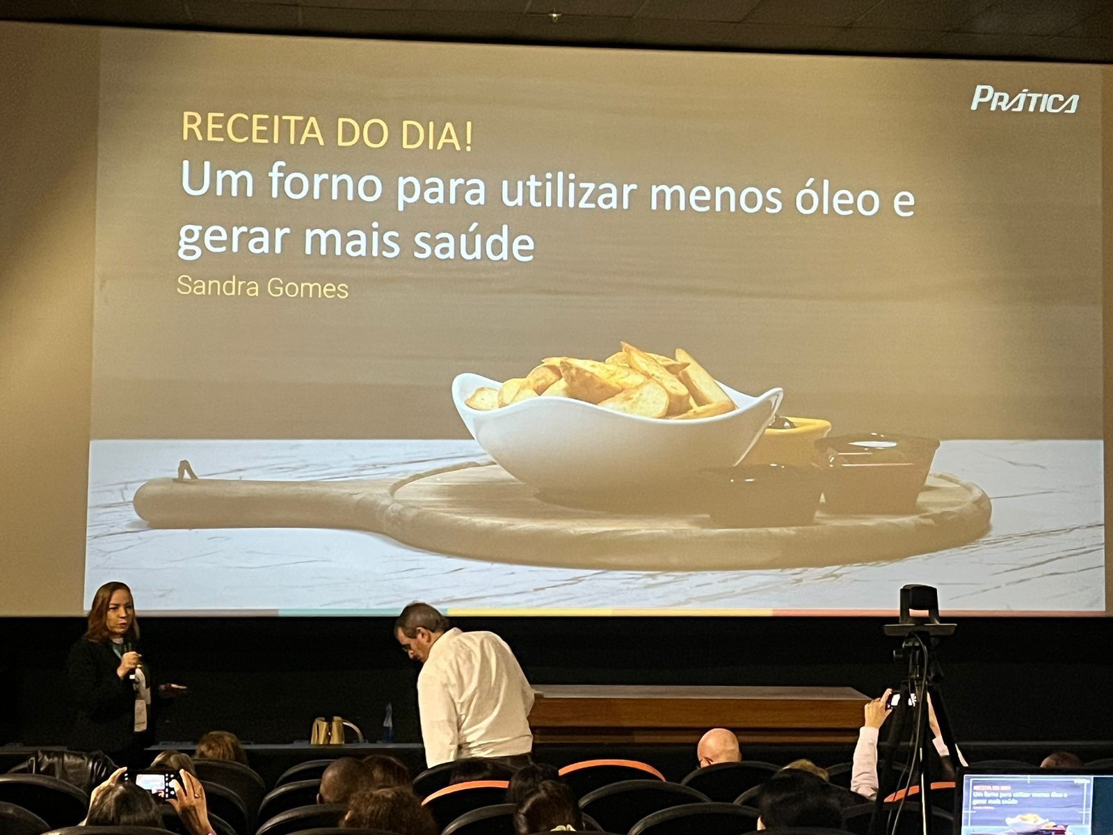 Um grupo de pessoas está sentado em frente a uma tela grande com uma tigela de comida sobre ela.
