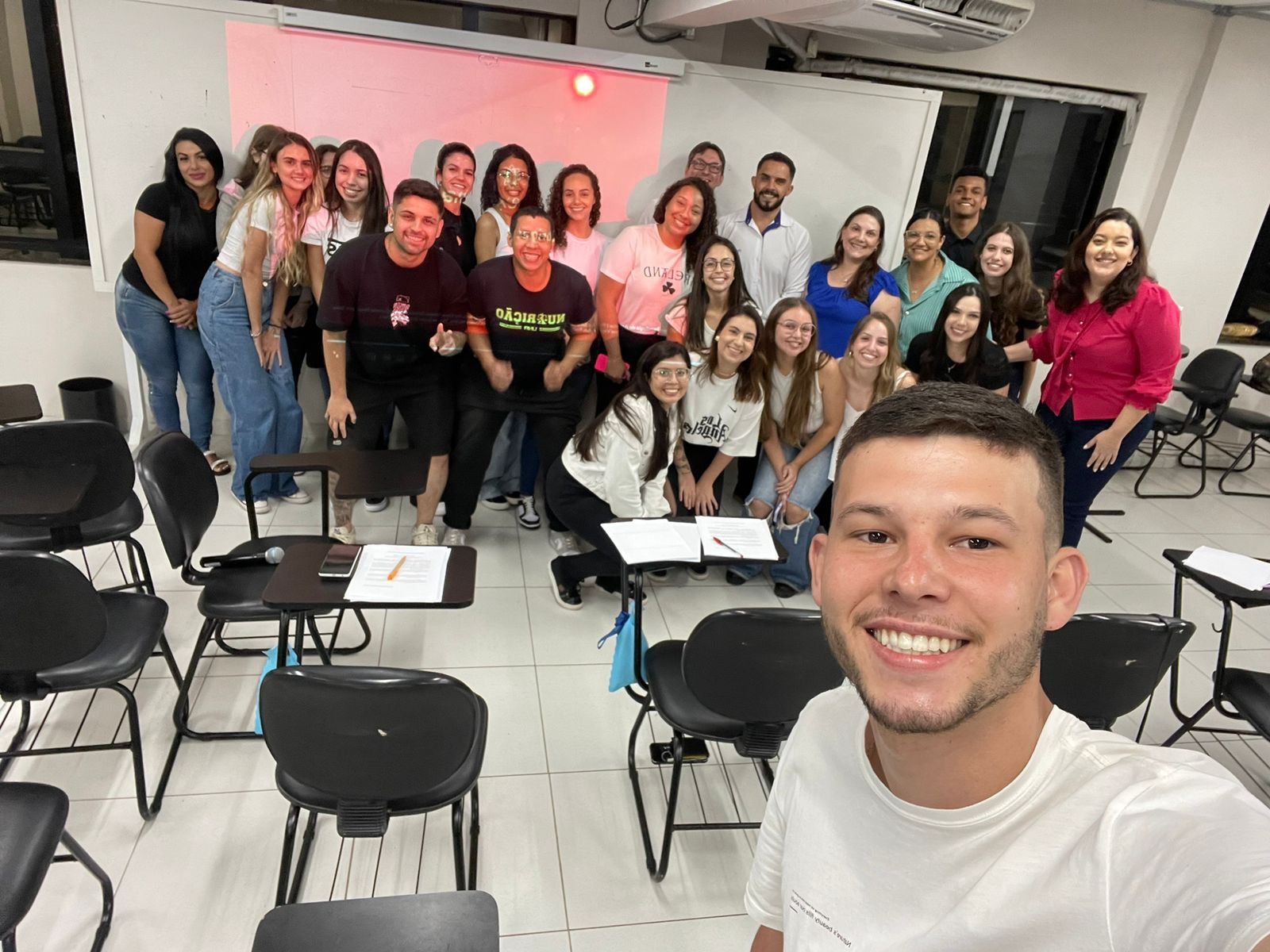 Um grupo de pessoas está posando para uma foto em uma sala de aula.