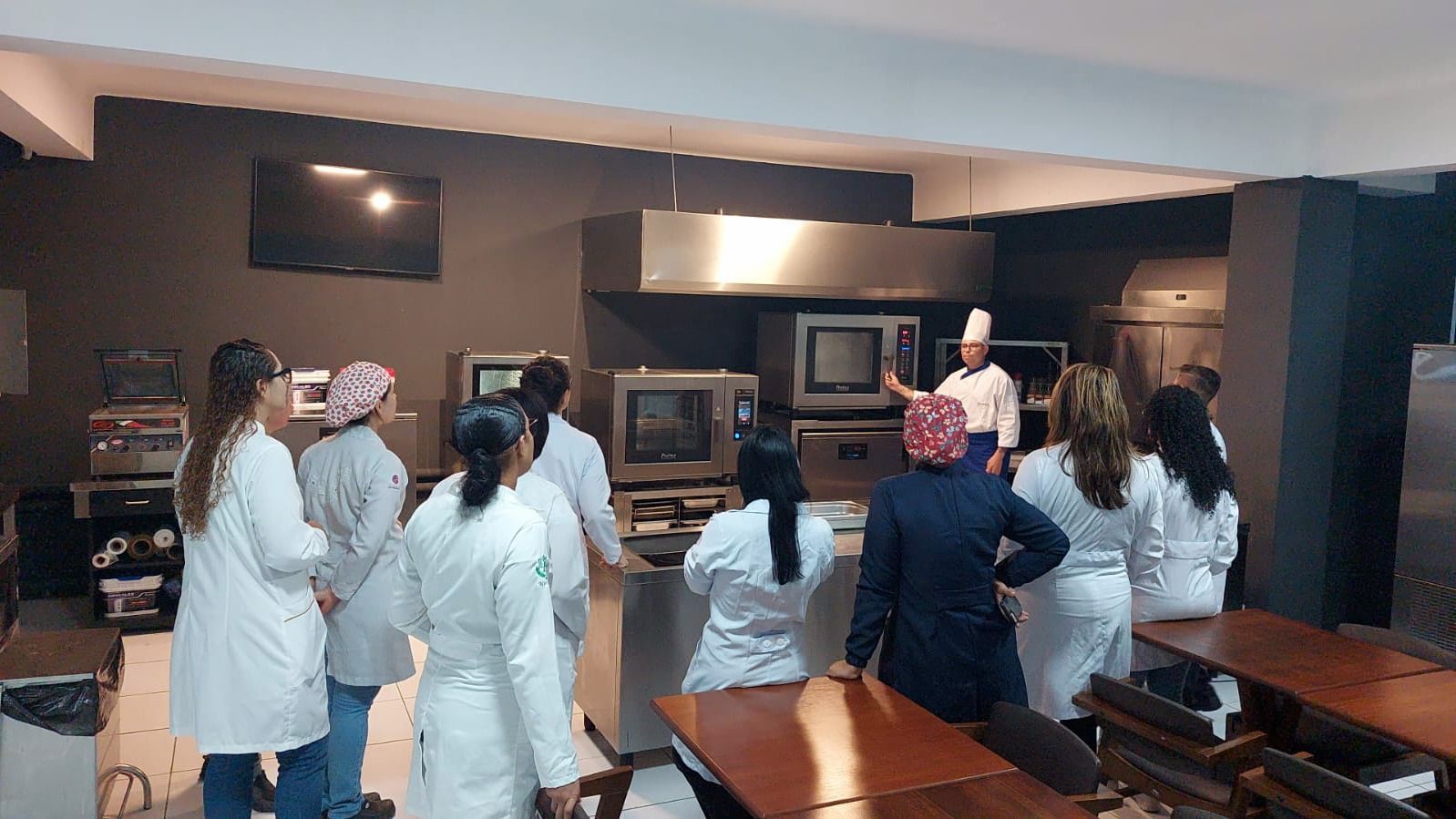 Um grupo de pessoas está em uma cozinha olhando para um chef.