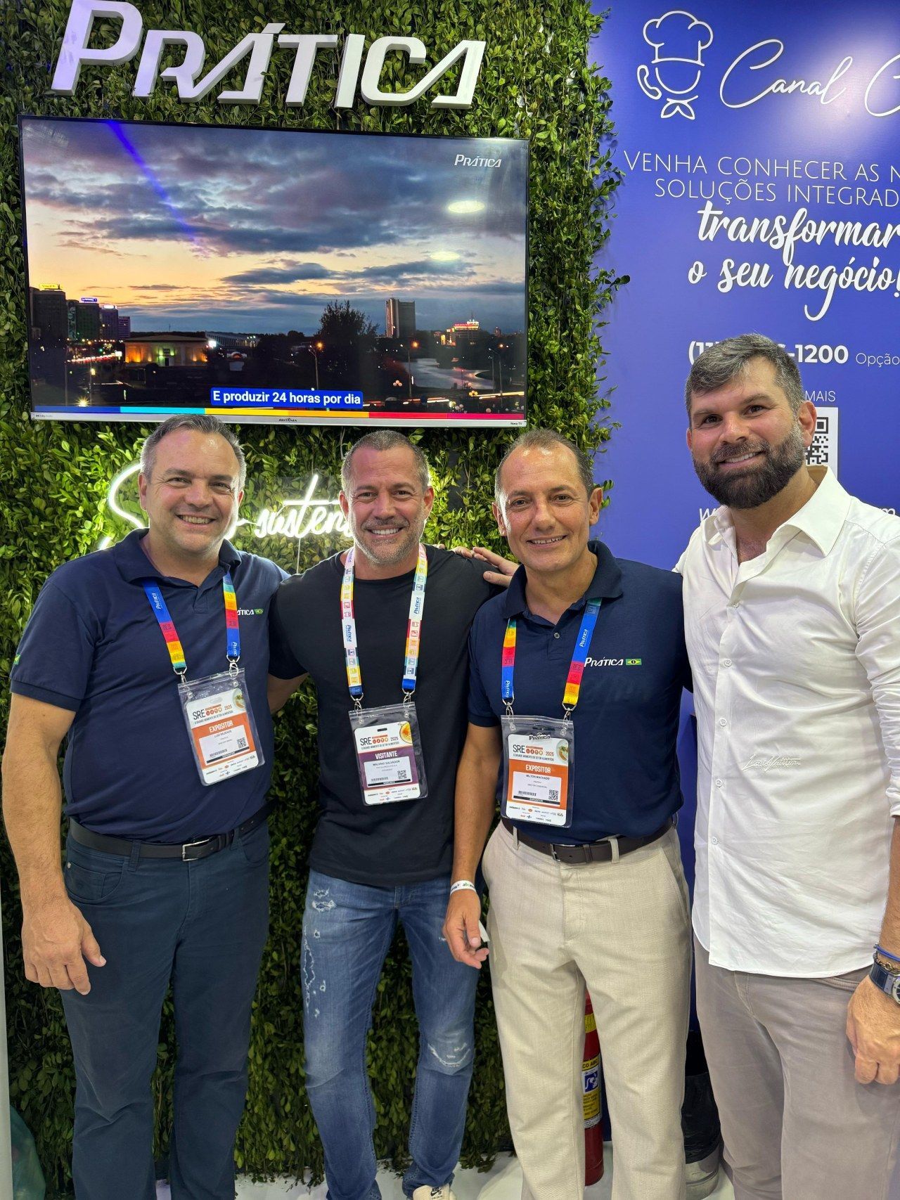 Um grupo de homens está posando para uma foto em frente a uma TV.