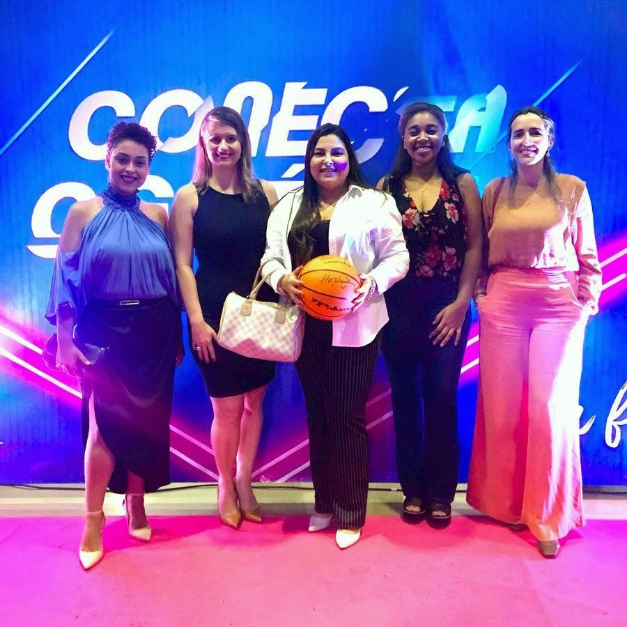 Um grupo de mulheres está posando para uma foto em frente a uma parede que diz comeca