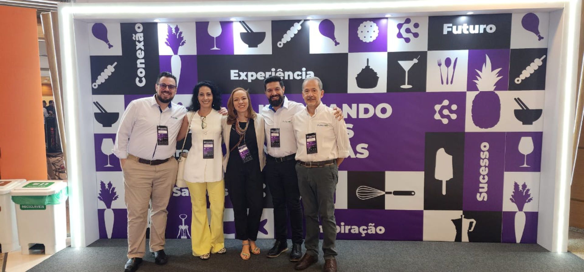 Um grupo de pessoas está posando para uma foto em frente a uma parede roxa.