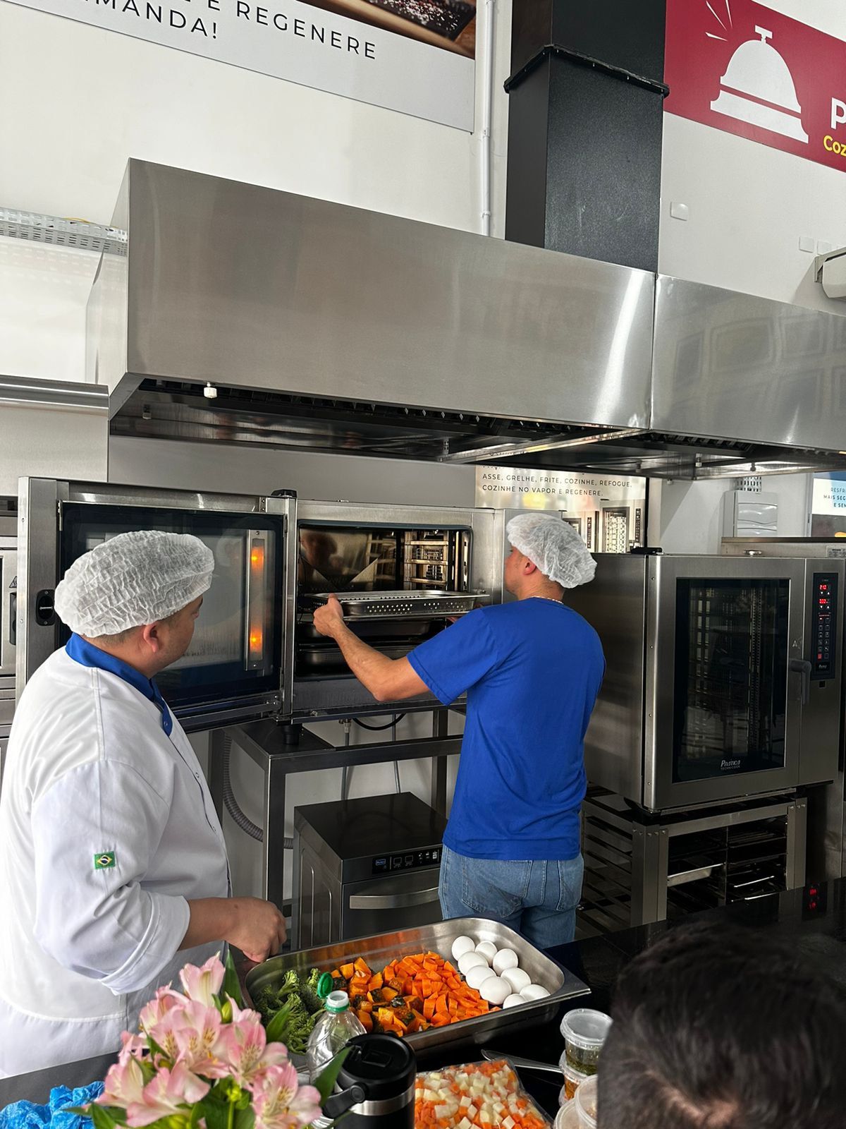Dois homens estão trabalhando em uma cozinha e um deles está colocando comida no forno.