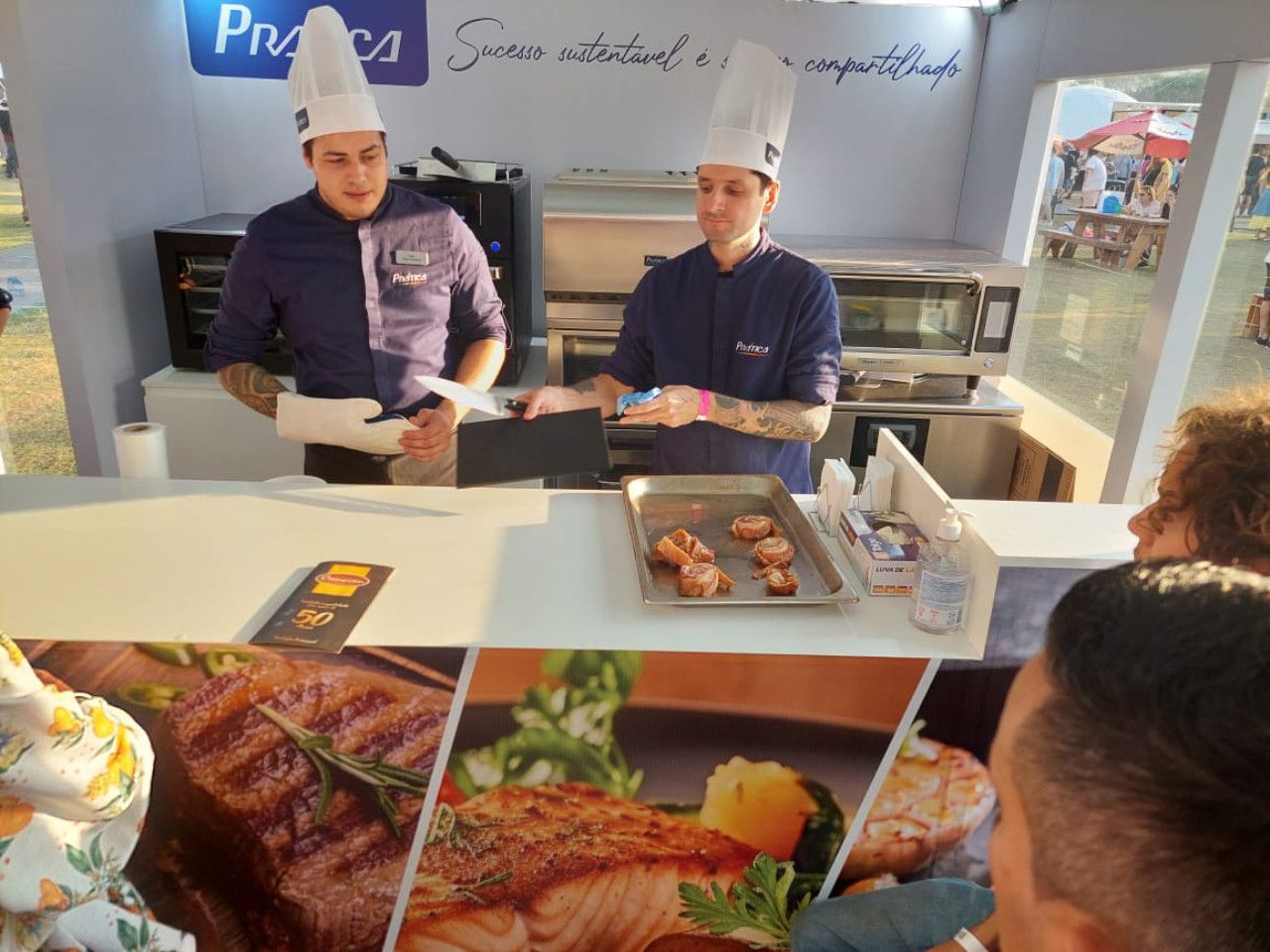 Dois chefs preparam comida em frente a uma placa que diz praca