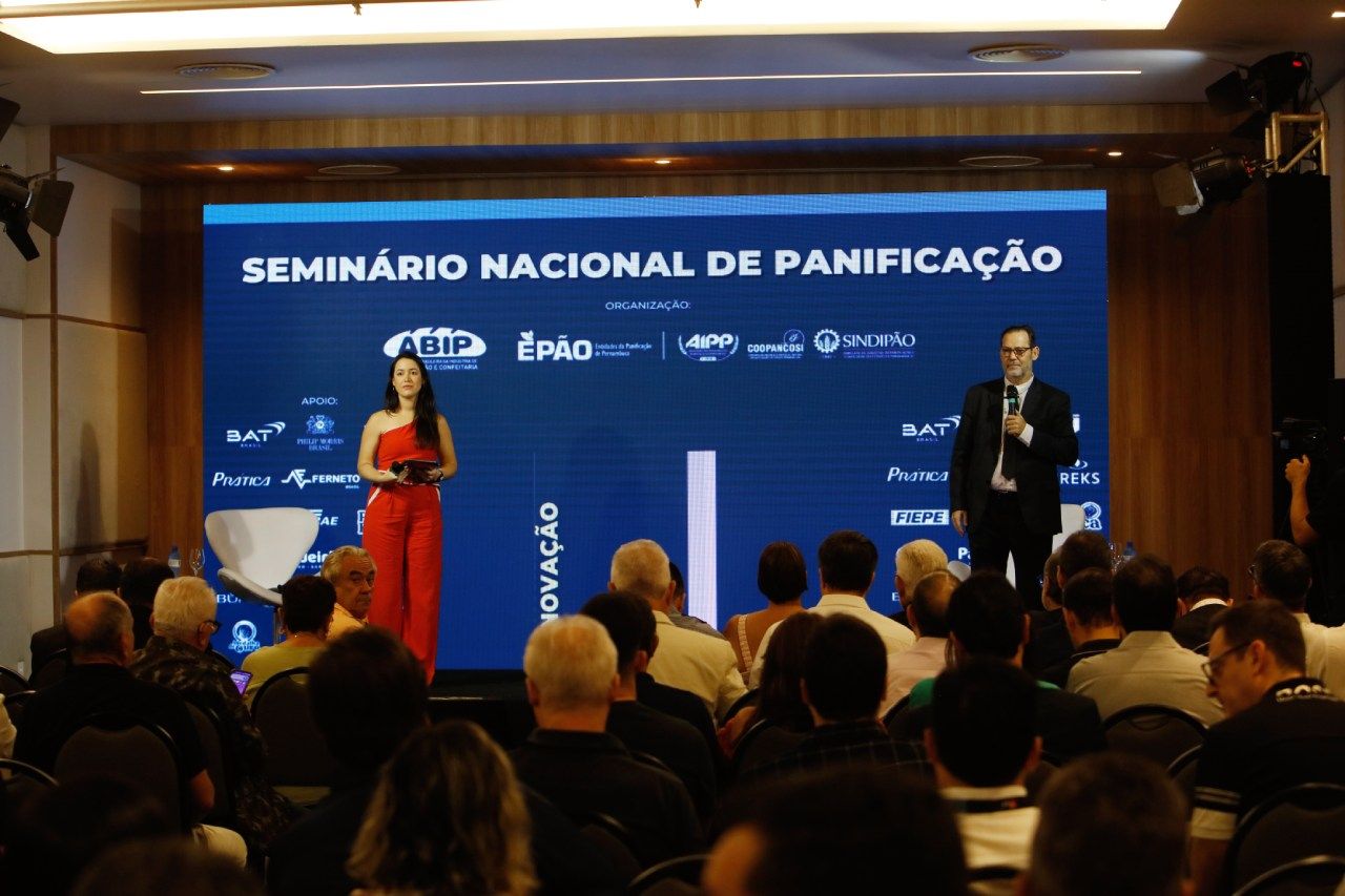 Um grupo de pessoas está sentado em frente a uma tela que diz seminário nacional de panificação