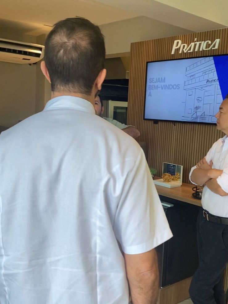 Um homem de camisa branca está parado em frente a uma TV.