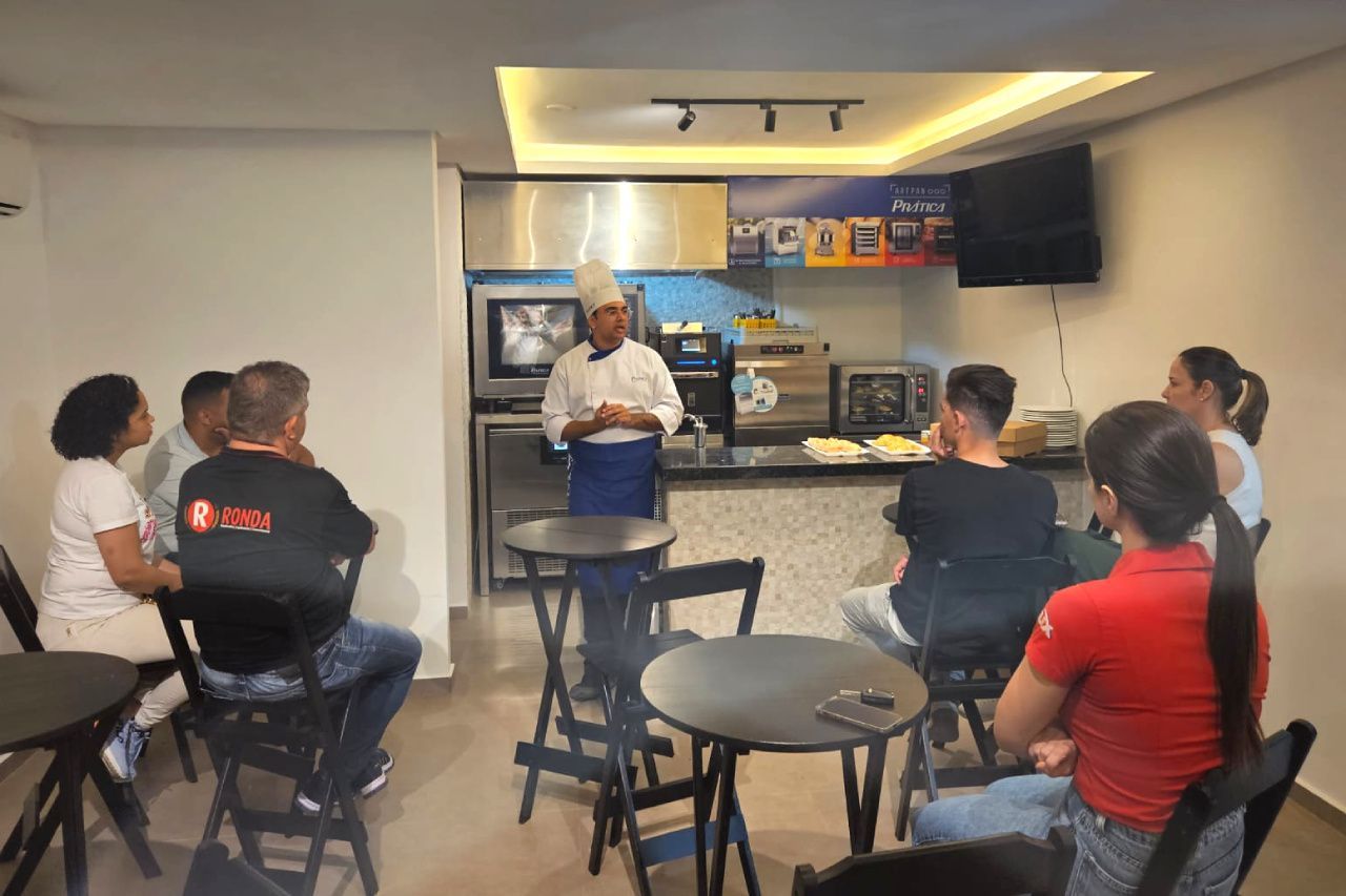Um grupo de pessoas está sentado em mesas em uma sala com um chef fazendo uma apresentação.