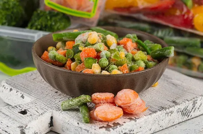 Uma tigela de vegetais congelados está sobre uma mesa de madeira.
